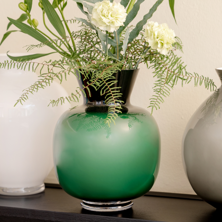 The large, bulbous glass vase "Anna" in bottle green with white flowers.